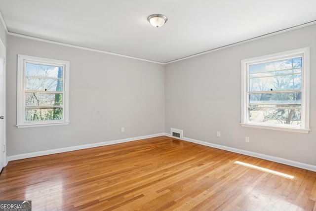 unfurnished room featuring healthy amount of natural light, baseboards, crown molding, and light wood-type flooring