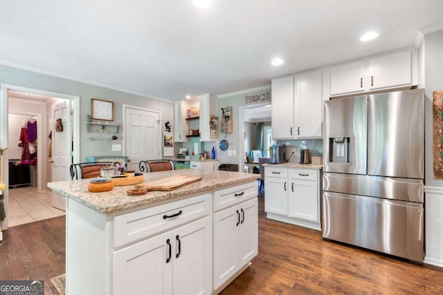 kitchen with stainless steel fridge, white cabinets, a kitchen island, ornamental molding, and dark wood-style flooring