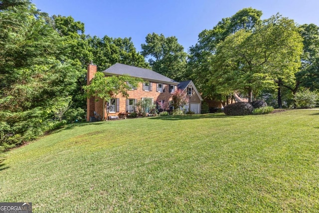 view of front of home featuring a chimney, a front yard, an attached garage, and brick siding