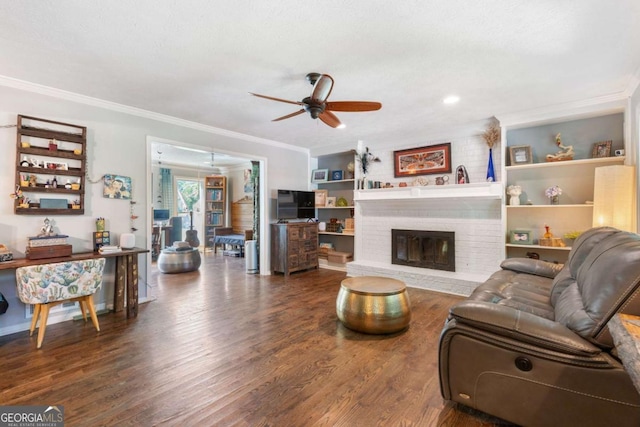 living area featuring a ceiling fan, crown molding, wood finished floors, and a brick fireplace