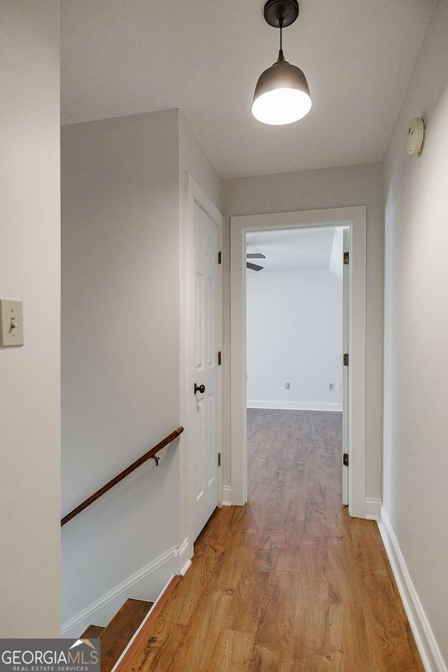 hallway with light wood-style floors, an upstairs landing, and baseboards