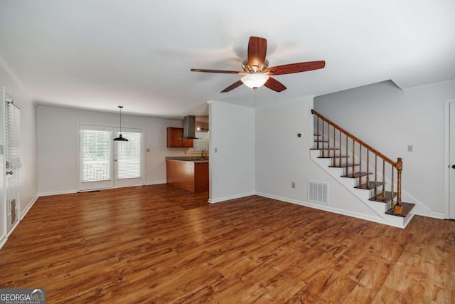 unfurnished living room with wood finished floors, ceiling fan, stairway, baseboards, and a sink