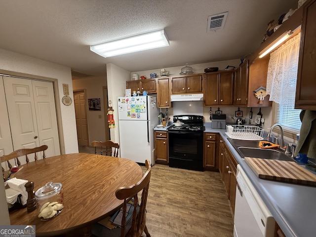 kitchen featuring white appliances, under cabinet range hood, a sink, light wood finished floors, and a textured ceiling