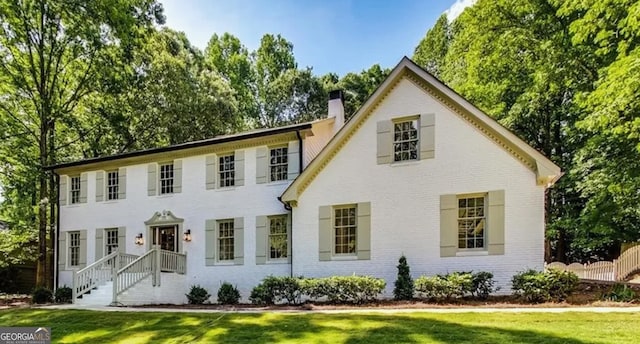 colonial home featuring a chimney, brick siding, and a front lawn