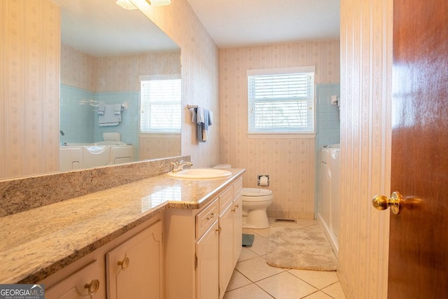 bathroom with independent washer and dryer, wallpapered walls, tile patterned floors, plenty of natural light, and toilet