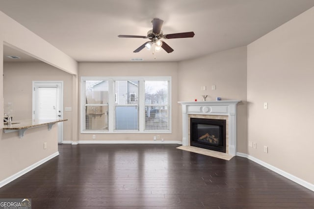 unfurnished living room featuring wood-type flooring, ceiling fan, a high end fireplace, and baseboards