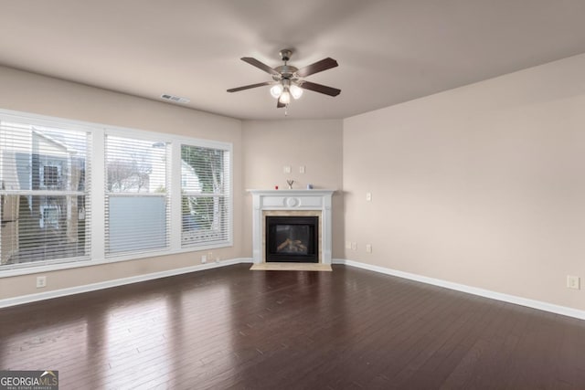 unfurnished living room with dark wood-type flooring, ceiling fan, baseboards, and a fireplace with flush hearth