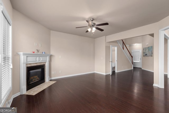unfurnished living room with wood finished floors, a ceiling fan, a high end fireplace, baseboards, and stairway