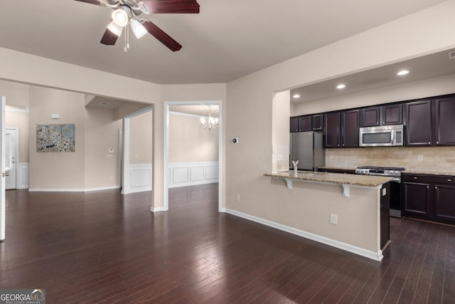 kitchen with appliances with stainless steel finishes, a chandelier, a ceiling fan, a kitchen breakfast bar, and light stone countertops