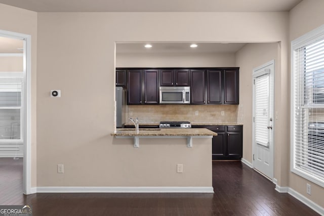 kitchen featuring stainless steel microwave, light stone countertops, tasteful backsplash, range, and dark wood-style flooring