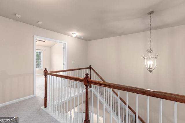 corridor with an upstairs landing, a chandelier, carpet flooring, and baseboards