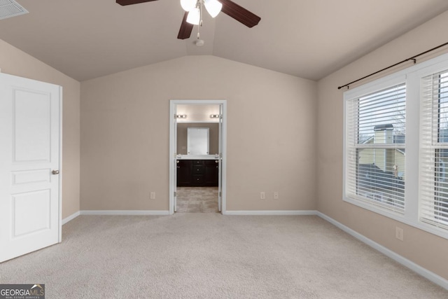 unfurnished bedroom featuring light colored carpet, lofted ceiling, baseboards, connected bathroom, and ceiling fan