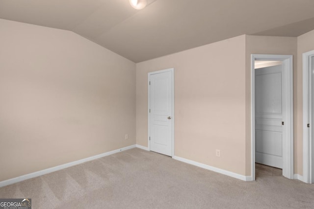 unfurnished bedroom featuring light colored carpet, baseboards, and lofted ceiling