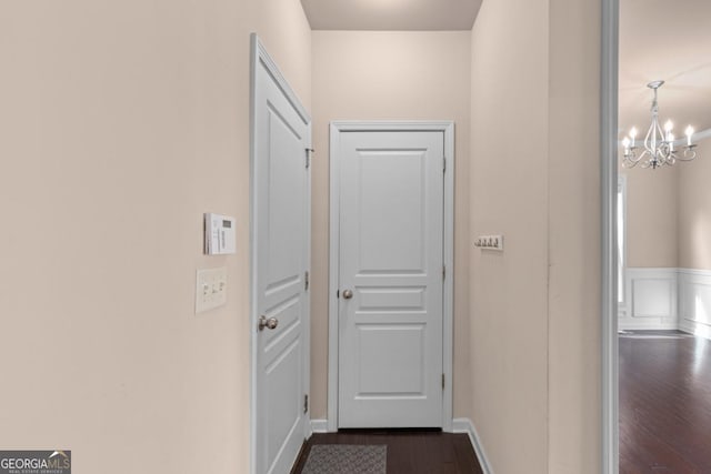 hallway with dark wood-type flooring, a chandelier, and baseboards