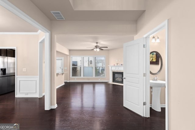 unfurnished living room featuring ceiling fan, wood finished floors, a fireplace with flush hearth, and wainscoting