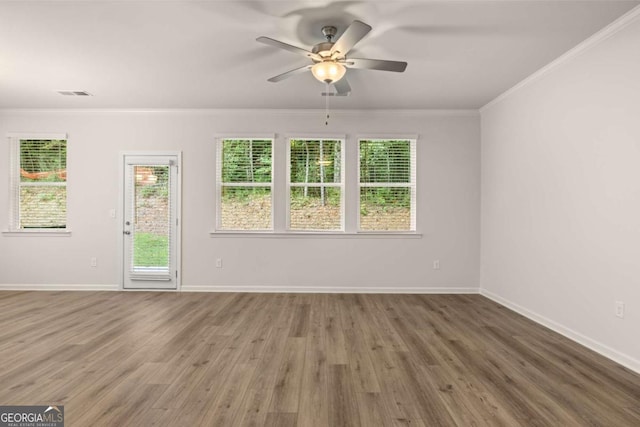 empty room featuring wood finished floors, ornamental molding, a ceiling fan, healthy amount of natural light, and baseboards