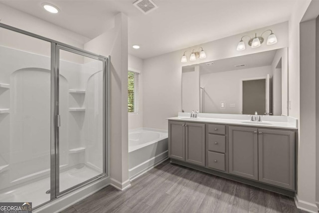 bathroom with wood finished floors, a stall shower, a garden tub, double vanity, and baseboards