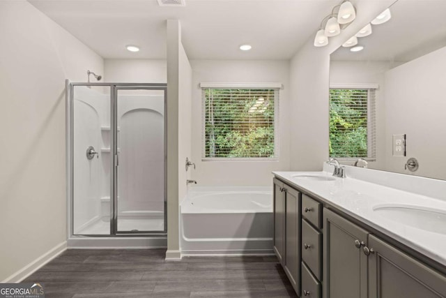 bathroom featuring a shower stall, a bath, wood finished floors, baseboards, and double vanity