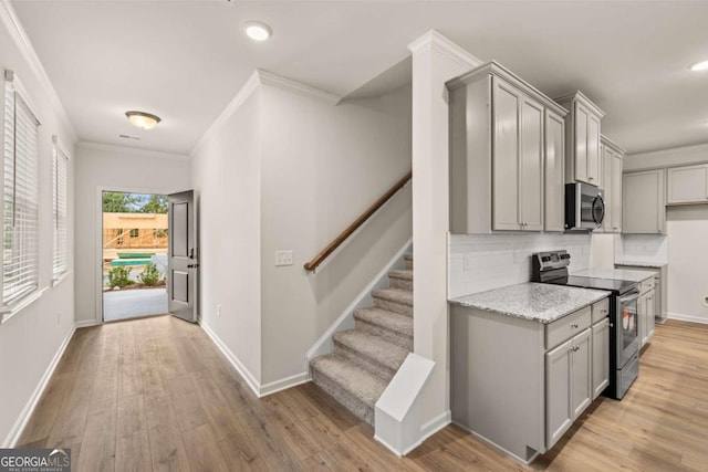 kitchen featuring appliances with stainless steel finishes, gray cabinetry, tasteful backsplash, light wood-style flooring, and ornamental molding