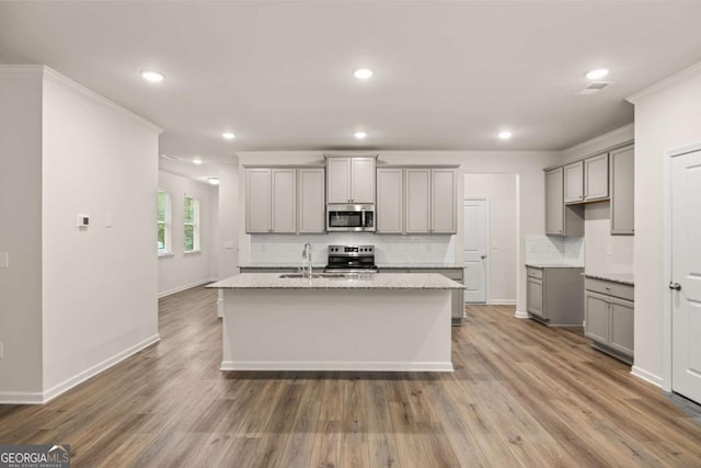 kitchen with gray cabinets, stainless steel appliances, backsplash, a center island with sink, and crown molding