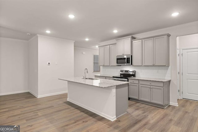 kitchen with appliances with stainless steel finishes, gray cabinets, a sink, crown molding, and a kitchen island with sink