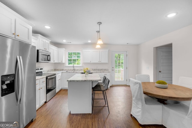 kitchen featuring stainless steel appliances, white cabinets, a breakfast bar, a sink, and recessed lighting