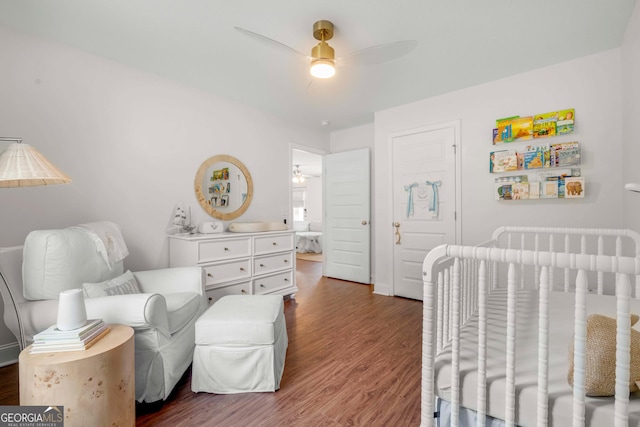 bedroom featuring wood finished floors, a nursery area, and a ceiling fan