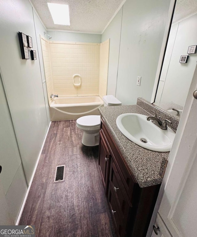 full bathroom with wood finished floors, toilet, vanity, a textured ceiling, and washtub / shower combination