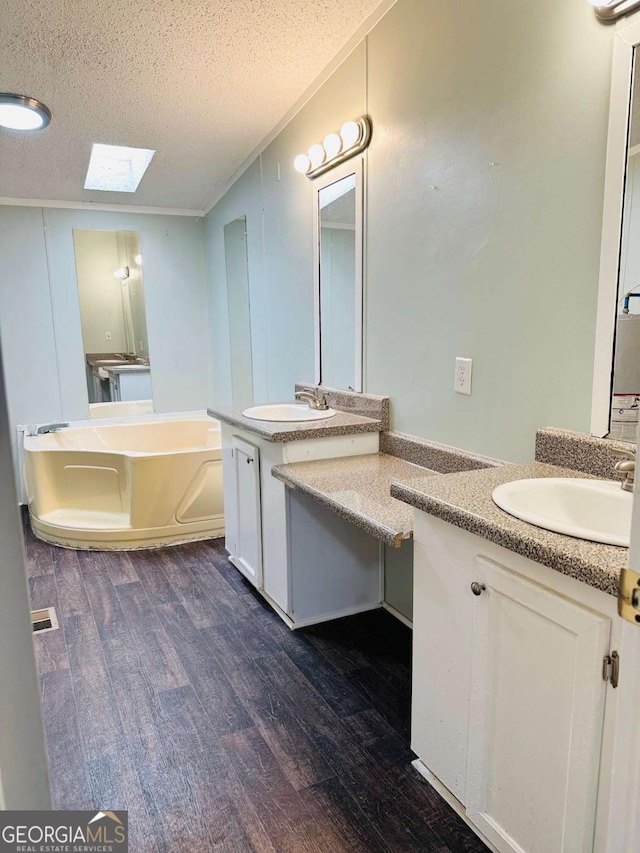 full bath featuring wood finished floors, a skylight, a textured ceiling, two vanities, and ornamental molding