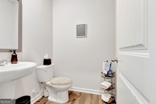 half bathroom with wood finished floors, toilet, baseboards, and a sink