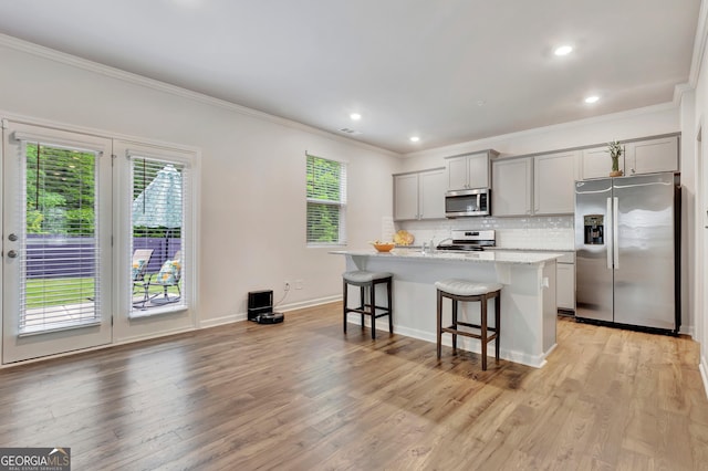 kitchen featuring appliances with stainless steel finishes, gray cabinets, a breakfast bar, crown molding, and a kitchen island with sink
