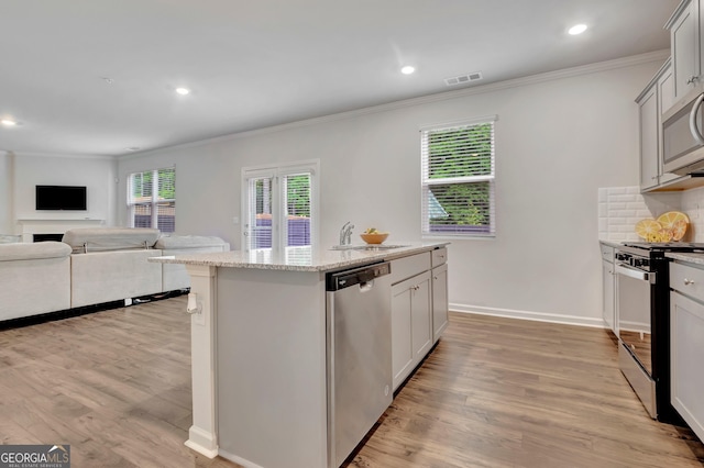 kitchen featuring appliances with stainless steel finishes, crown molding, a kitchen island with sink, light wood-style floors, and tasteful backsplash
