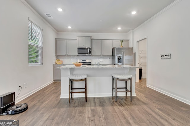 kitchen featuring appliances with stainless steel finishes, gray cabinets, a breakfast bar, an island with sink, and crown molding