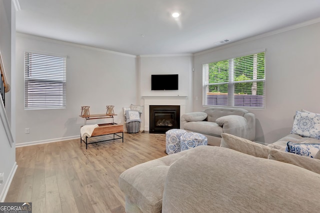 living area featuring light wood-style flooring, crown molding, a glass covered fireplace, and baseboards