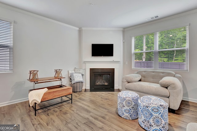 living room featuring wood finished floors, crown molding, a fireplace with flush hearth, and baseboards
