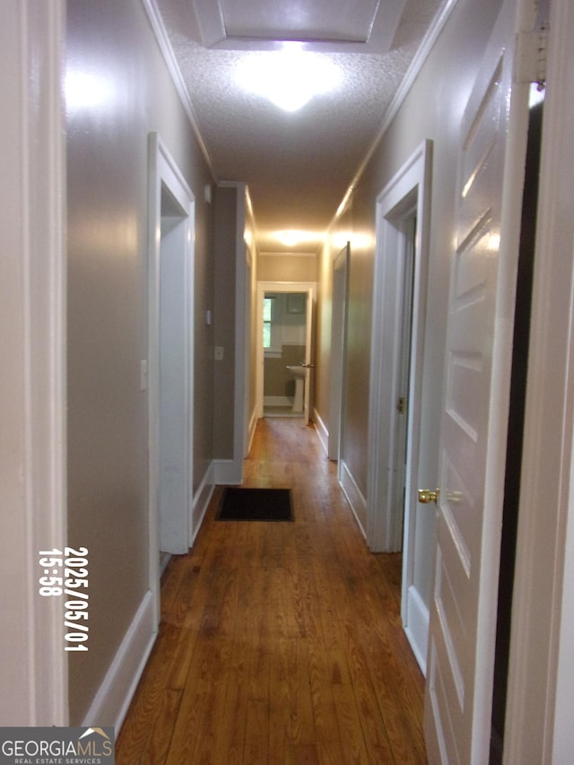 corridor featuring wood finished floors, crown molding, baseboards, and a textured ceiling