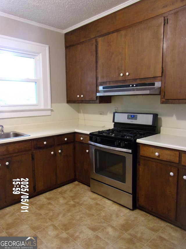 kitchen featuring gas range, under cabinet range hood, light countertops, ornamental molding, and a textured ceiling