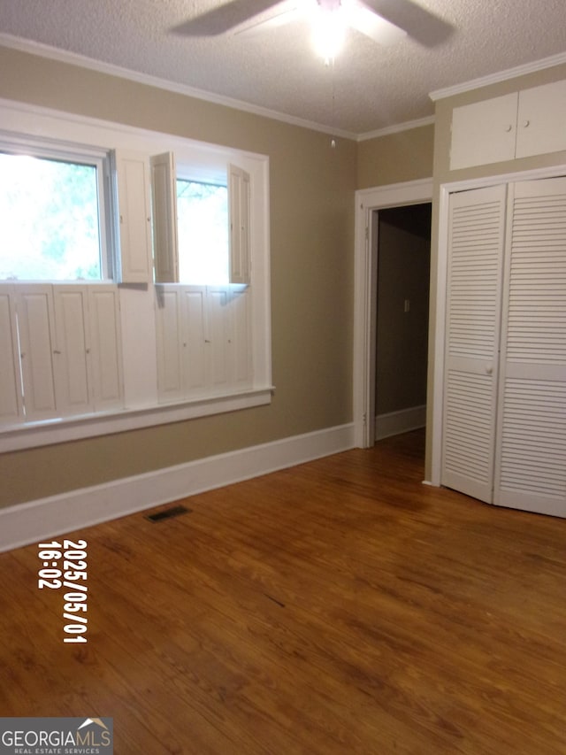 unfurnished bedroom with wood finished floors, multiple windows, crown molding, a textured ceiling, and a closet
