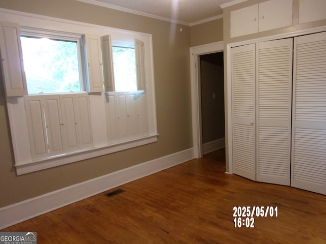 unfurnished bedroom with crown molding, wood finished floors, a closet, and baseboards