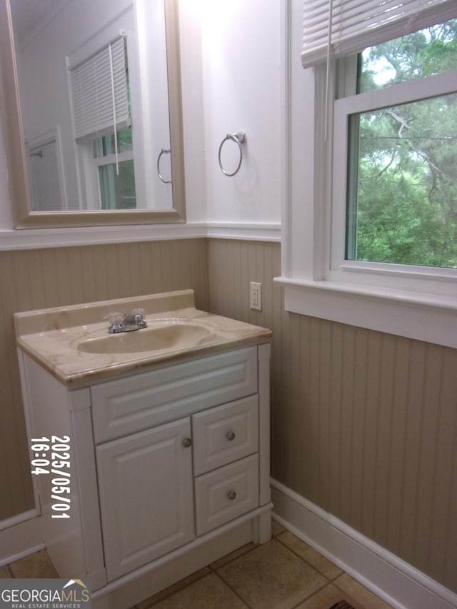 bathroom with healthy amount of natural light, tile patterned floors, vanity, and a wainscoted wall