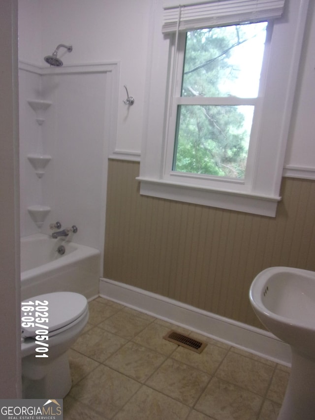 full bath featuring washtub / shower combination, wainscoting, toilet, and tile patterned floors