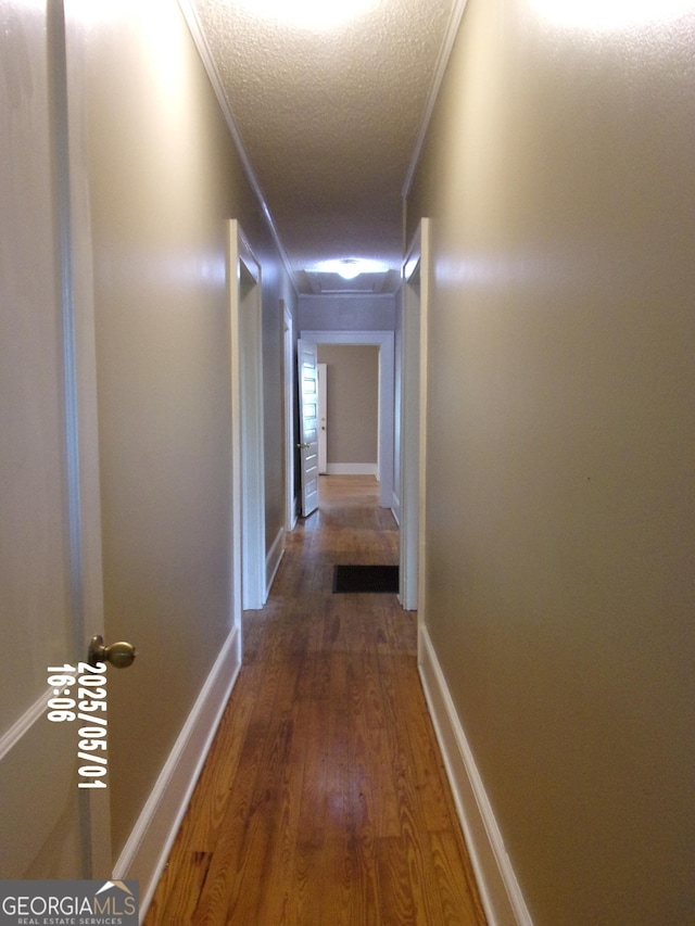 corridor featuring a textured ceiling, wood finished floors, crown molding, and baseboards