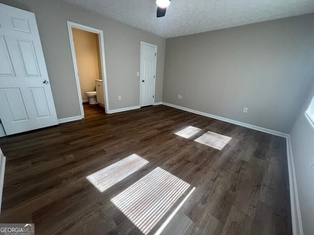 unfurnished bedroom with dark wood-style floors, baseboards, ensuite bath, and a ceiling fan