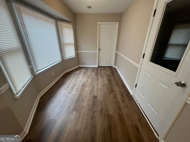 unfurnished dining area featuring dark wood-style flooring and baseboards