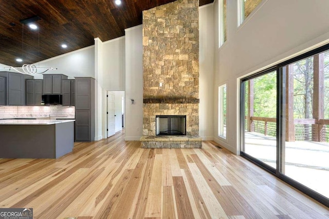 unfurnished living room featuring wood ceiling, high vaulted ceiling, light wood-style flooring, a stone fireplace, and recessed lighting