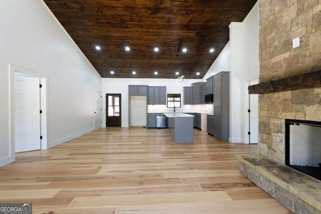 unfurnished living room with wood ceiling, light wood-style floors, high vaulted ceiling, a fireplace, and a sink