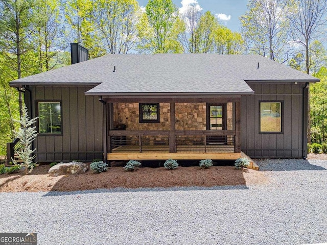 view of front facade featuring board and batten siding, covered porch, a shingled roof, and a chimney
