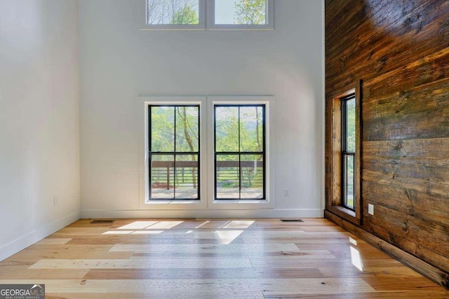 spare room featuring wood finished floors, wooden walls, a towering ceiling, and baseboards