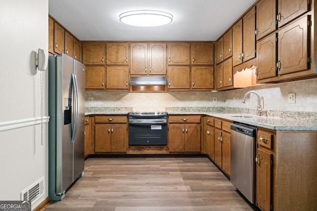 kitchen featuring appliances with stainless steel finishes, under cabinet range hood, a sink, brown cabinets, and light wood-style floors