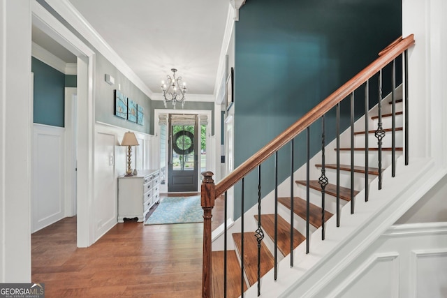 entryway with a decorative wall, ornamental molding, a chandelier, wood finished floors, and a wainscoted wall